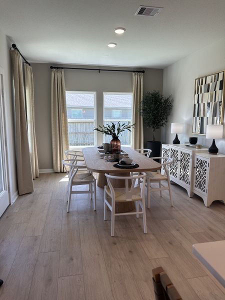 A modern dining area with a wooden table, elegant chairs, soft curtains, and chic decor, inviting warmth and style.