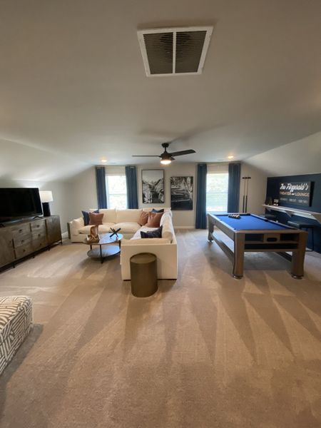 A cozy entertainment room with plush carpet, sectional sofa, pool table, and stylish decor for a relaxing lounge experience.
