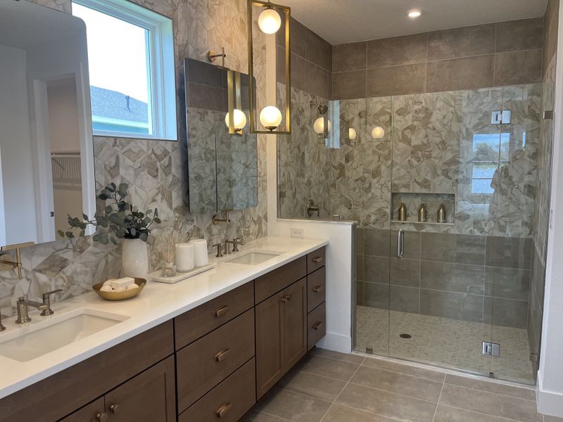 A luxurious bathroom with dual sinks, a glass-enclosed shower, and elegant tile accents creating a serene spa-like atmosphere.