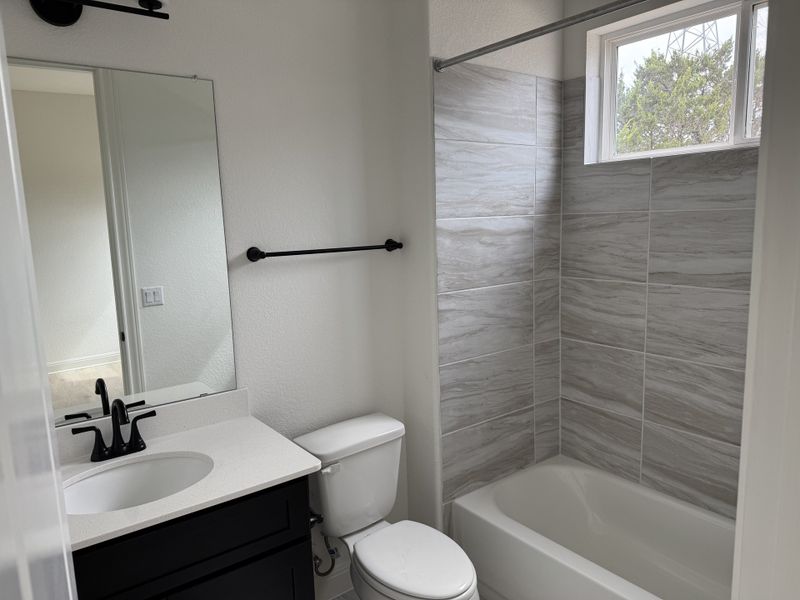 A modern bathroom with sleek gray tile shower, black faucet, white countertop, and ample natural light.