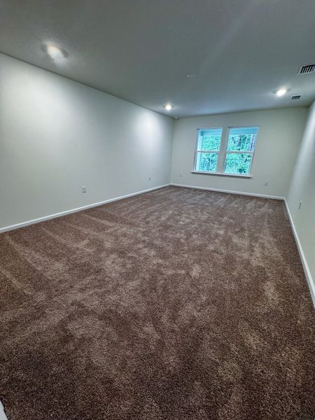A spacious room with plush carpet, soft white walls, and recessed lighting, offering a cozy ambiance.