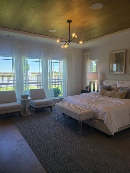 A serene bedroom featuring a cozy bed, elegant seating, and warm lighting with large windows offering abundant natural light.