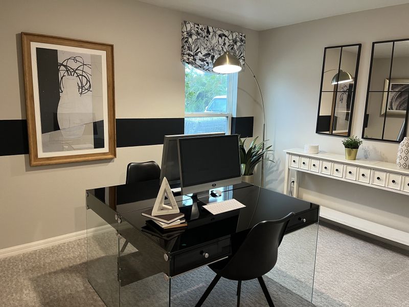 A modern office with a sleek black desk, stylish artwork, and ample natural light, perfect for productivity.