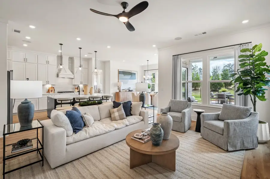 Open-concept living room with white sofa, round wood coffee table, and kitchen visible in background
