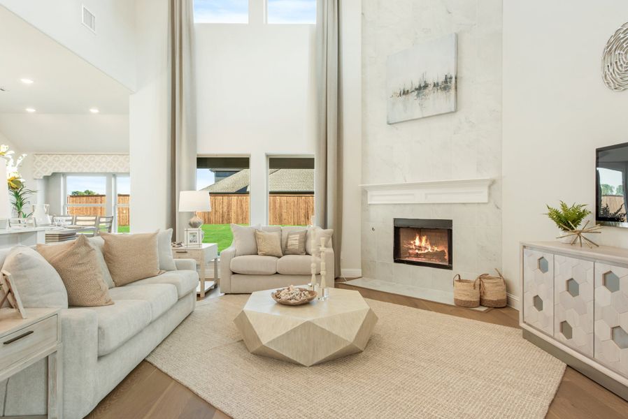 Living room with two-story ceiling, white fireplace, neutral sofas, and hardwood floors