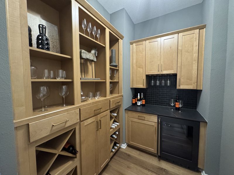 A charming home bar with warm wood cabinetry, wine storage, and a sleek mini-fridge against sophisticated gray walls.