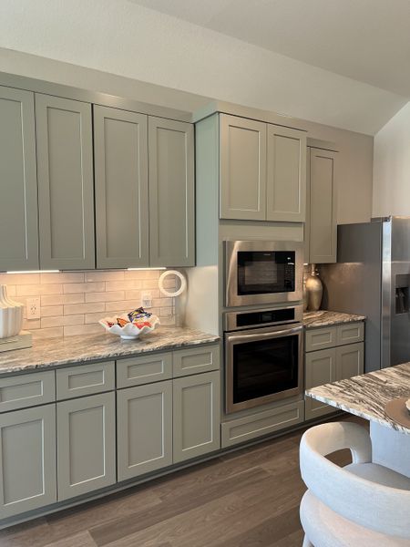 A modern kitchen with sleek gray cabinets, marble countertops, and stainless steel appliances.