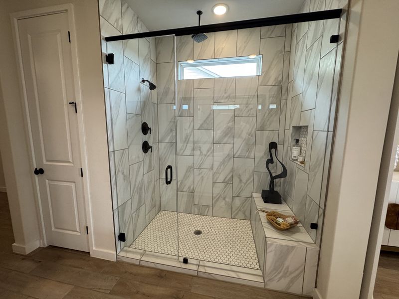 A modern shower with marble tiles, glass enclosure, and elegant black fixtures, featuring a stylish sculptural accent piece.