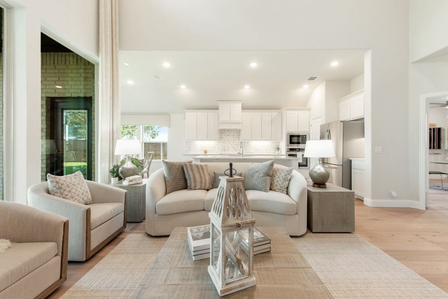 Open-concept living room with neutral furniture and hardwood floors, open to white kitchen with stainless appliances Open-concept living room with neutral furniture and hardwood floors, open to white kitchen with stainless appliances