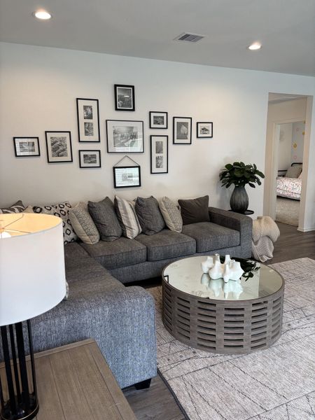 A cozy living room with a gray sectional sofa, framed art collage, chic round coffee table, and soft neutral tones.