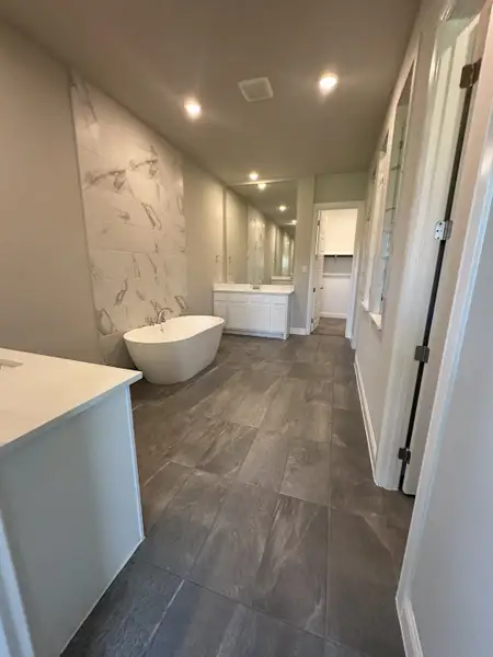 A sleek bathroom featuring a freestanding tub, marble accent wall, and spacious vanities under recessed lighting. A sleek bathroom featuring a freestanding tub, marble accent wall, and spacious vanities under recessed lighting.