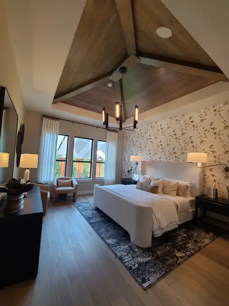 A luxurious bedroom featuring a textured accent wall, elegant lighting, and a wooden ceiling design with cozy seating.