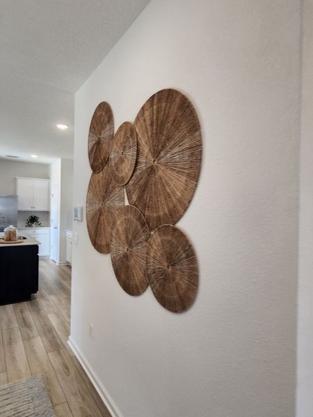 Modern hallway with wood flooring and artistic woven wall decor. Bright and inviting atmosphere with a view into the kitchen.