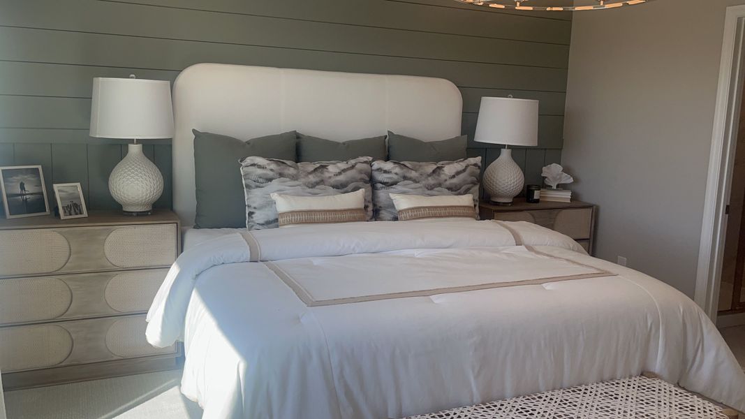 A cozy bedroom with a plush white bed, green accent wall, elegant lamps, and stylish decor.