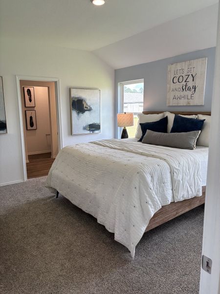 A cozy bedroom featuring a neutral palette, decorative artwork, plush bedding, and soft carpeting, creating a serene retreat.