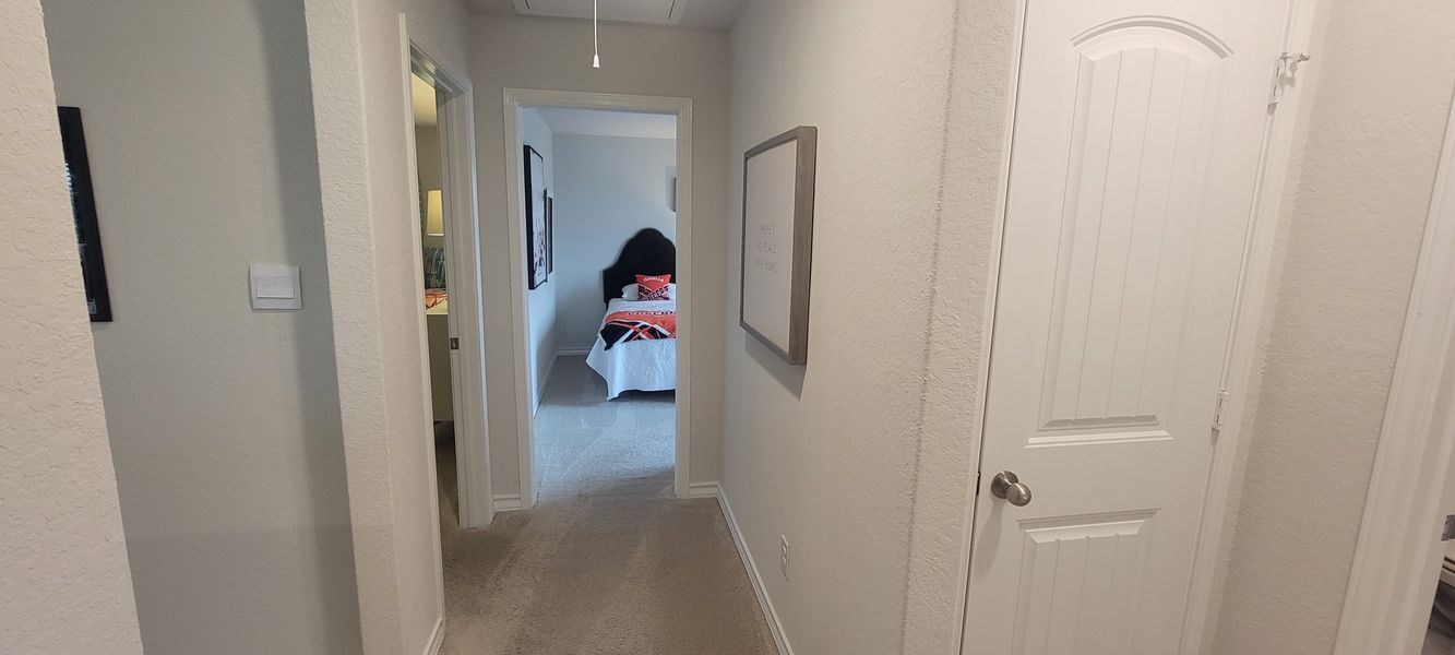 A cozy hallway leading to a bedroom with neutral tones, soft carpet, and a black headboard with vibrant bedding.