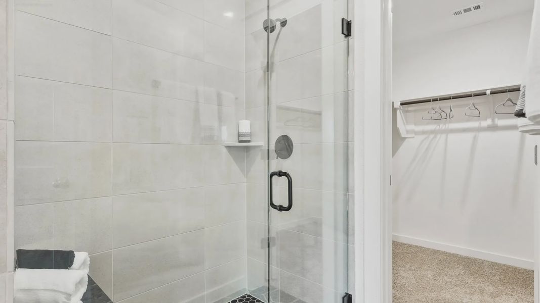 Elegant glass shower with sleek black fixtures and hexagon tile floor, adjacent to walk-in closet, Simpson Crossing.