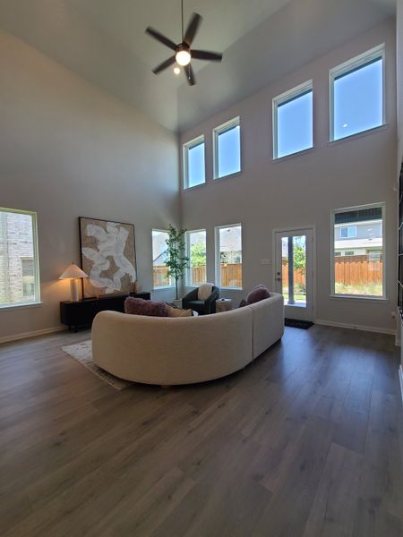 A spacious living room with a vaulted ceiling, large windows, elegant artwork, and a cozy curved sofa arrangement.
