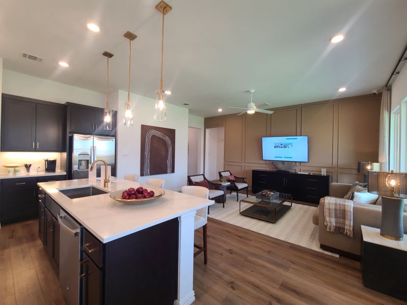 An elegant open-plan kitchen and living room with dark cabinets, a quartz island, and modern lighting. An elegant open-plan kitchen and living room with dark cabinets, a quartz island, and modern lighting.