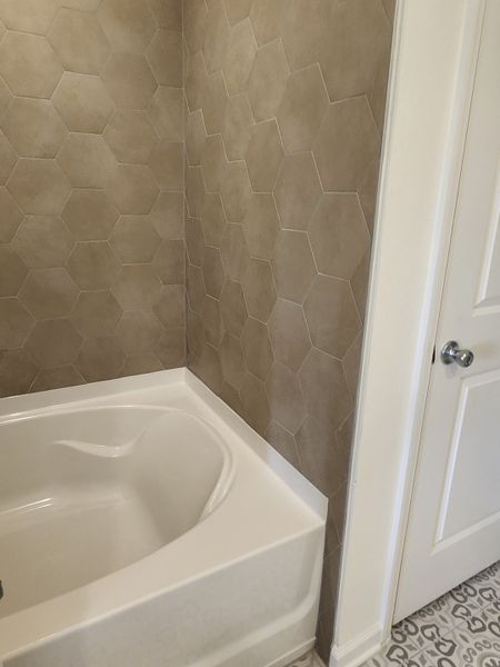 A modern bathroom with hexagonal beige tiles and a sleek white bathtub, complemented by patterned floor tiles.