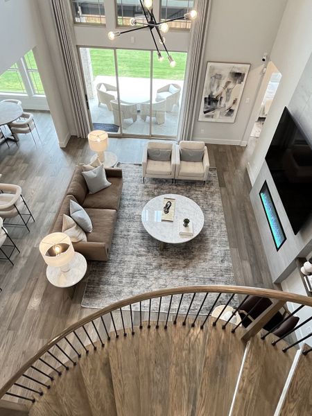A modern living area with stylish furniture, large windows, and a chic chandelier, viewed from a curved staircase. A modern living area with stylish furniture, large windows, and a chic chandelier, viewed from a curved staircase.