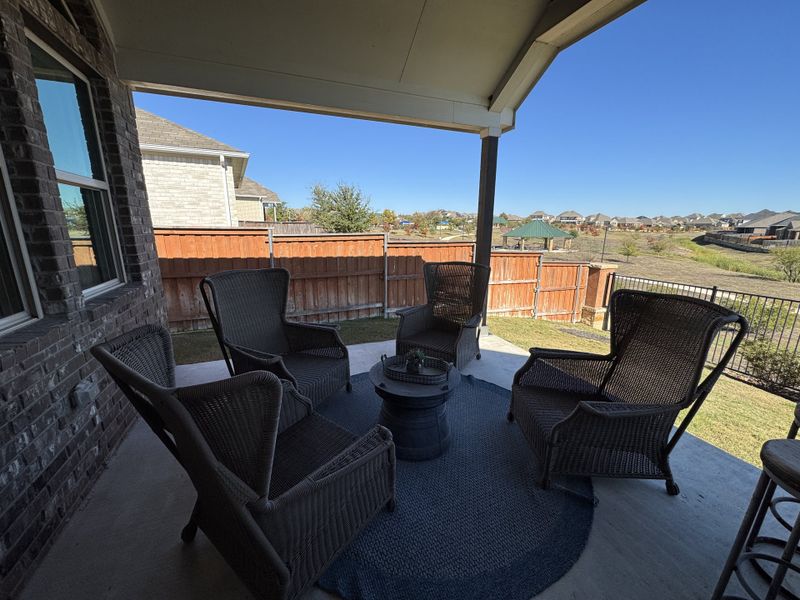 A cozy patio area with wicker chairs and a blue rug, offering a view of a landscaped backyard and neighborhood homes. A cozy patio area with wicker chairs and a blue rug, offering a view of a landscaped backyard and neighborhood homes.