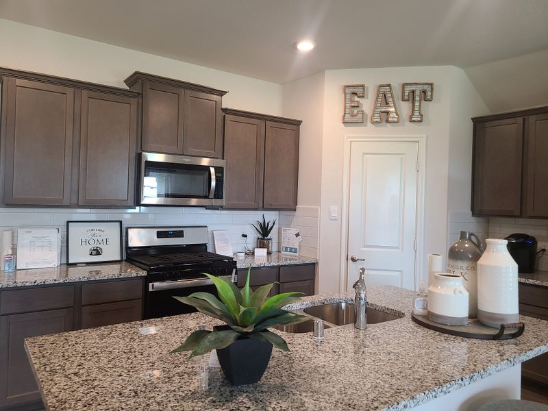 A modern kitchen with granite countertops, gray cabinets, stainless steel appliances, and warm decor elements.