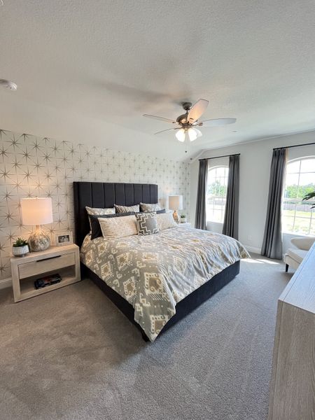 A modern bedroom with patterned accent wall, cozy bedding, and ample natural light from large windows. A modern bedroom with patterned accent wall, cozy bedding, and ample natural light from large windows.