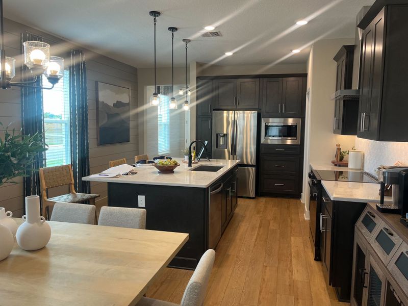 A modern kitchen with sleek cabinetry, stainless steel appliances, an island, and pendant lighting. Cozy dining area adjacent. A modern kitchen with sleek cabinetry, stainless steel appliances, an island, and pendant lighting. Cozy dining area adjacent.
