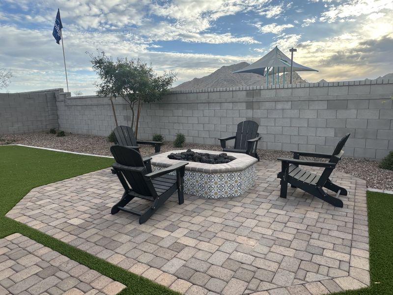 A charming fire pit area with black Adirondack chairs and a decorative stone base.