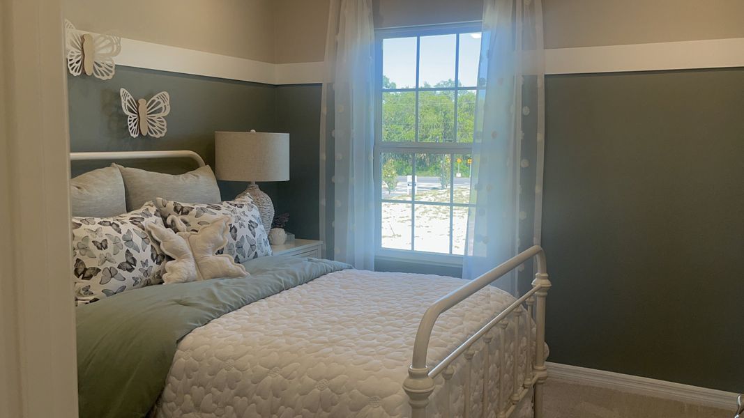 A cozy bedroom with a metal bed frame, butterfly-themed decor, and a window offering scenic views.