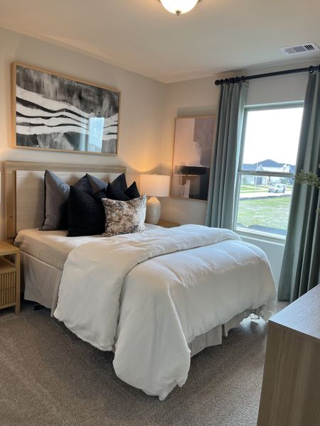 A cozy bedroom featuring elegant bedding, modern artwork, and a large window with soft drapery.