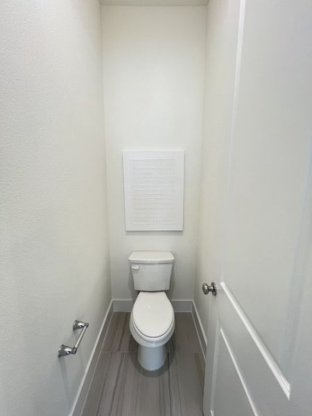 A compact powder room featuring gray floor tiles, a sleek white toilet, and minimalist design. A compact powder room featuring gray floor tiles, a sleek white toilet, and minimalist design.