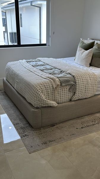 A cozy bedroom featuring a neutral-toned bed, soft linens, and a large window with natural light.