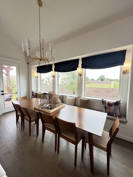 A cozy dining area featuring a wooden table, sleek chairs, elegant chandelier, and large windows with chic navy valances.