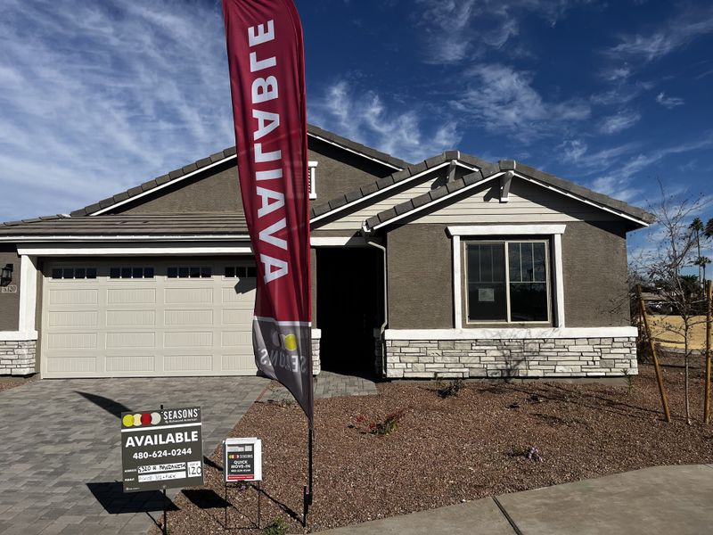 A stylish house with a light garage, stone accents, and and a paved driveway, set in a sunny neighborhood.