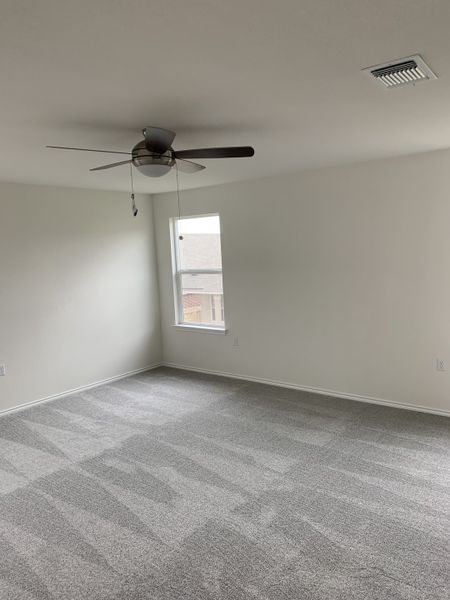 A spacious, light-filled room with fresh gray carpeting, modern ceiling fan, and a single window.