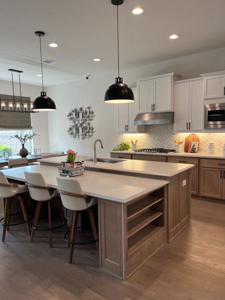 A modern kitchen with a large island, sleek black pendant lights, and elegant white cabinetry.
