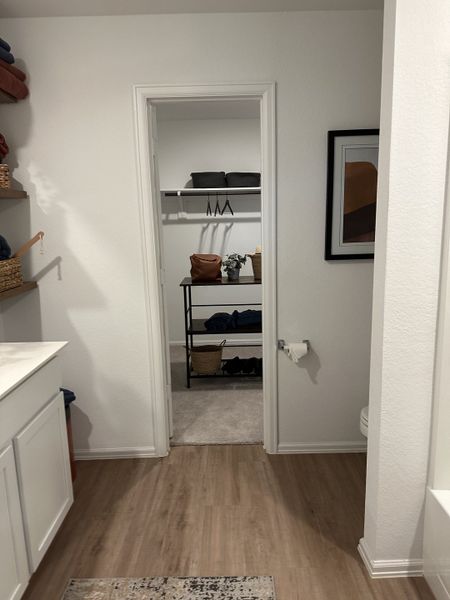A cozy bathroom with wood flooring, pristine white cabinets, and a view into an organized walk-in closet. A cozy bathroom with wood flooring, pristine white cabinets, and a view into an organized walk-in closet.
