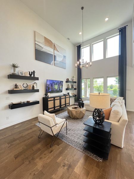 A spacious living room with high ceilings, elegant furnishings, a modern chandelier, and large windows filling the space with light.