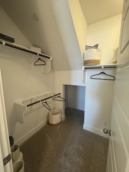 A cozy walk-in closet features plush carpeting, angled ceiling, open shelving, and wicker baskets for stylish storage.