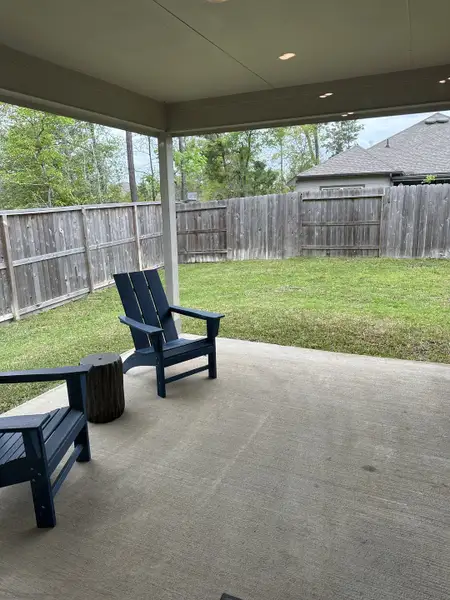 A cozy covered patio with blue Adirondack chairs and a private fenced backyard, perfect for relaxation. A cozy covered patio with blue Adirondack chairs and a private fenced backyard, perfect for relaxation.