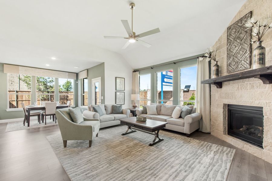 Open living room with stone fireplace, vaulted ceiling, ceiling fan, and dining area visible in background