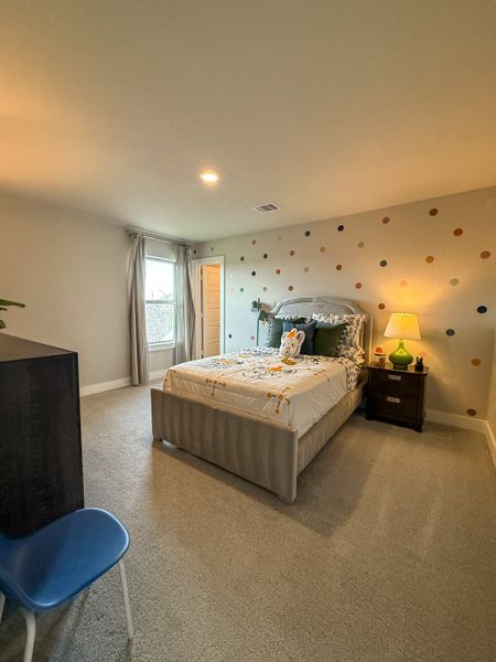 A cozy bedroom with a polka dot accent wall, neutral carpet, and soft lighting, featuring a stylish bed and bedside lamp.