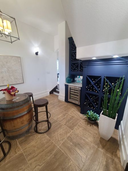 A chic wine nook featuring a blue wine rack, barrel table, stools, and elegant lighting, creating a cozy corner for relaxation. A chic wine nook featuring a blue wine rack, barrel table, stools, and elegant lighting, creating a cozy corner for relaxation.