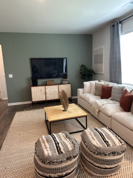 A cozy living room featuring a modern TV stand, plush sofa, patterned poufs, and earthy tones for a stylish ambiance.
