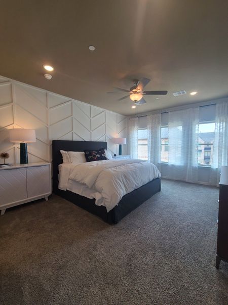 A cozy bedroom with a textured accent wall, plush carpeting, and large windows allowing natural light to fill the space.