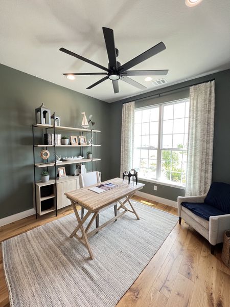 A cozy home office featuring a wooden desk, large window, and stylish bookshelf against a green accent wall.