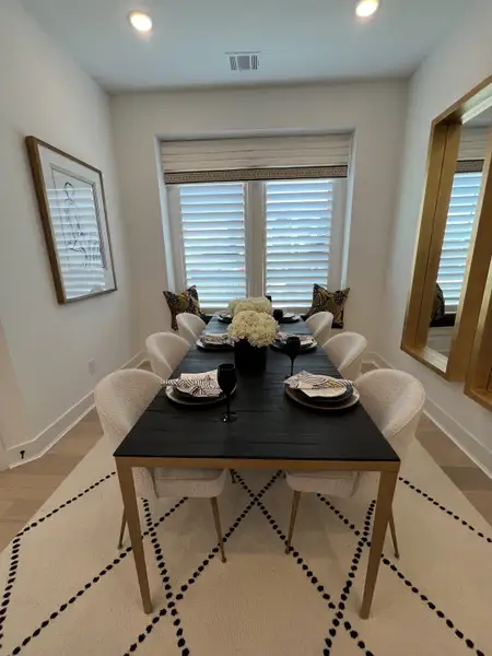 A chic dining room featuring a sleek black table, cozy upholstered chairs, and elegant decor with natural light.