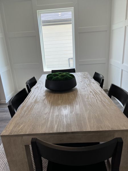 A modern dining area with a sleek wooden table, black chairs, and a decorative centerpiece, illuminated by natural light.